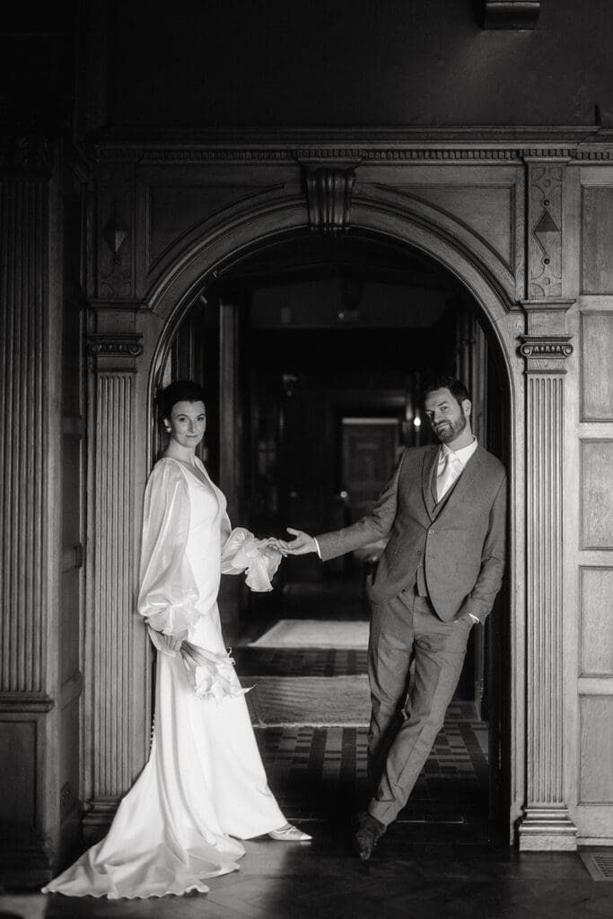 Trouwen in een kasteel: Elegante kasteelbruiloft in de Ardennen, bruid en bruidegom in de deuropening en houden elkaars hand vast, door artistieke bruidsfotograaf in Nederland